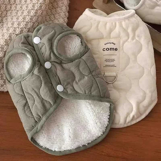 Two pet coats, one green and one white, on a wooden surface.